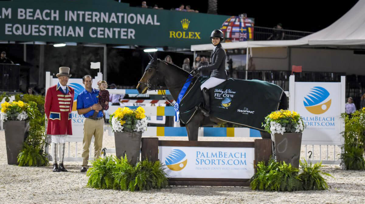 Adrienne Sternlicht galloped to victory aboard Just A Gamble in the $209,000 Holiday & Horses Grand Prix CSI 4* presented by Palm Beach County Sports Commission. Pictured with ringmaster Steve Rector, and Scott Glinski with his daughter of PBCSC. (©ESP)