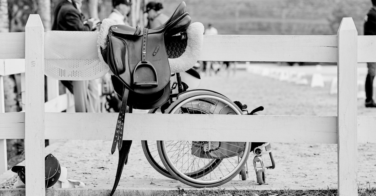 A wheelchair parked beside a fence with a saddle on it.