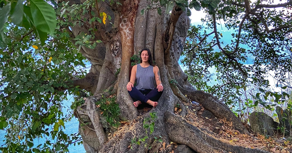A woman meditating at t he base of a large tree.