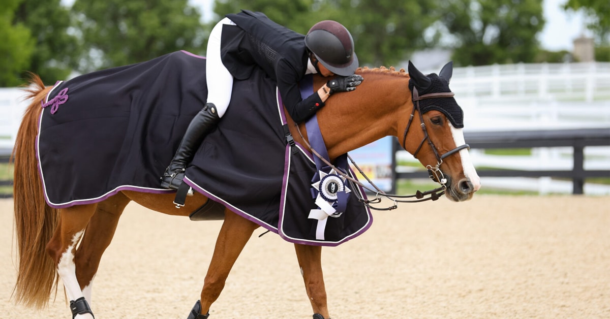 A woman patting her horse after winning a grand prix.