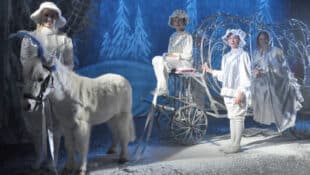 A white pony posing with a carriage and actors.