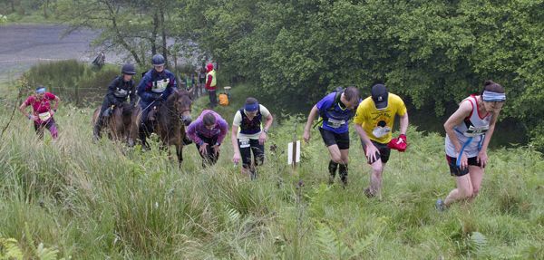 People and horses racing up a hill.