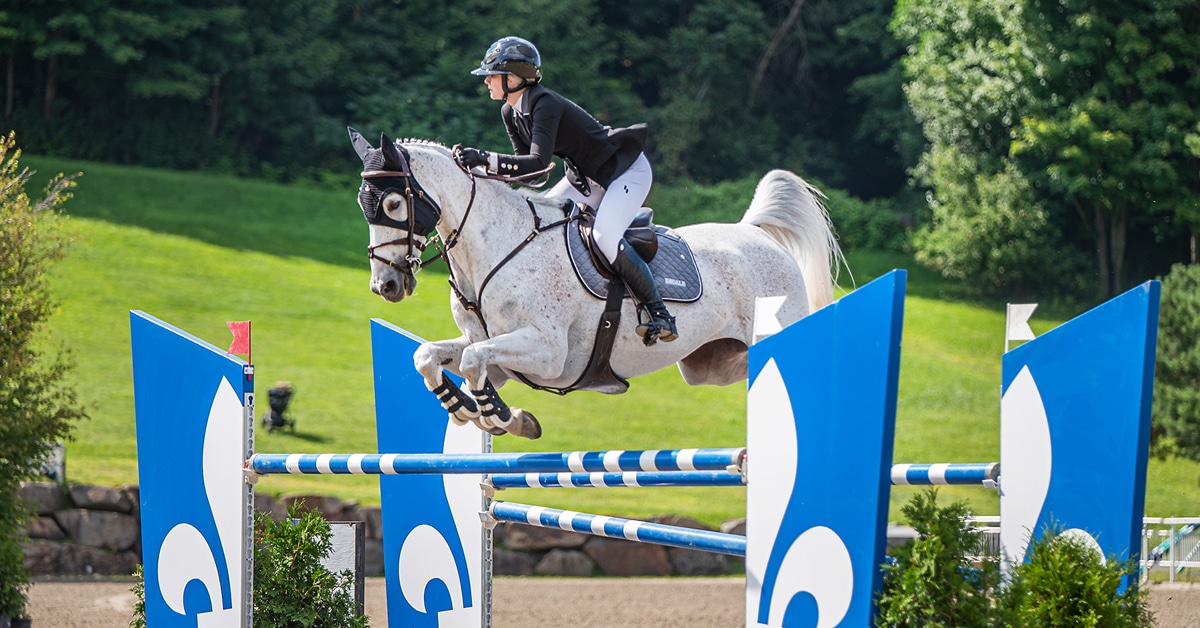 A woman jumping a grey horse over a fence at Bromont.