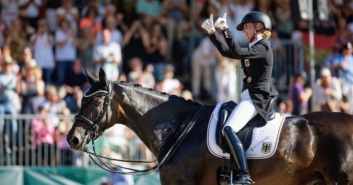 A woman on a dressage horse giving a thumbs-up.