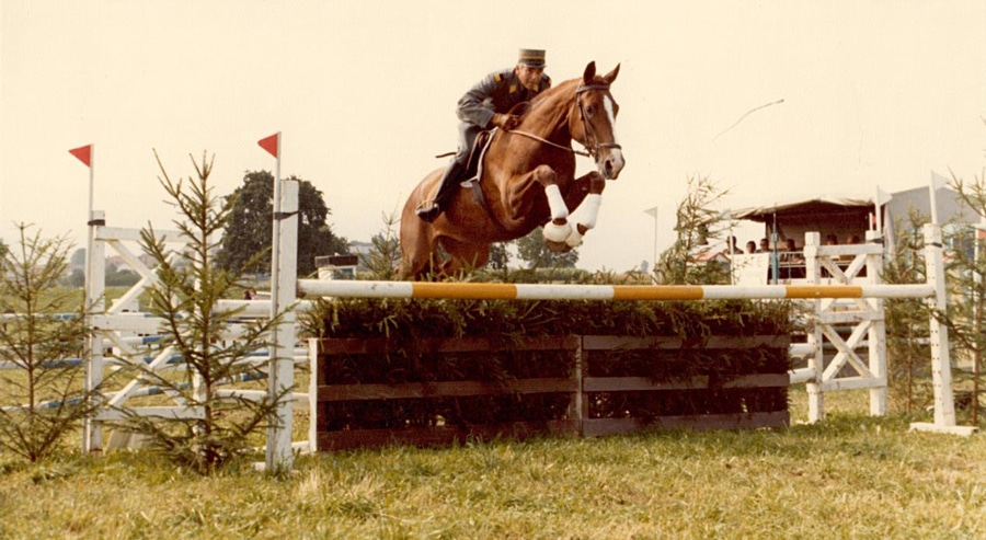 An old photo of a horse and rider jumping a fence.