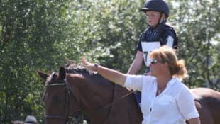 A woman coaching a young rider on a horse.