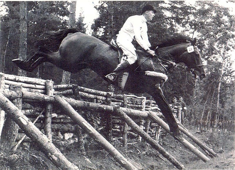 An old black and white photo of a horse and rider jumping.