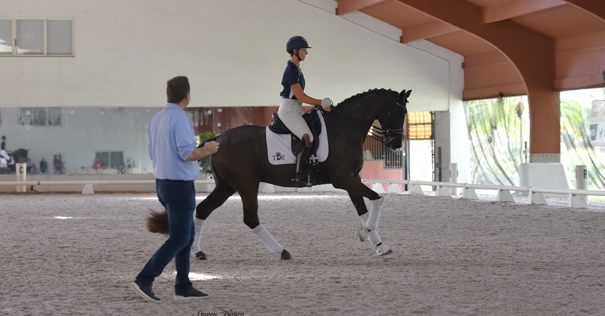 A man instructing a rider in an arena.