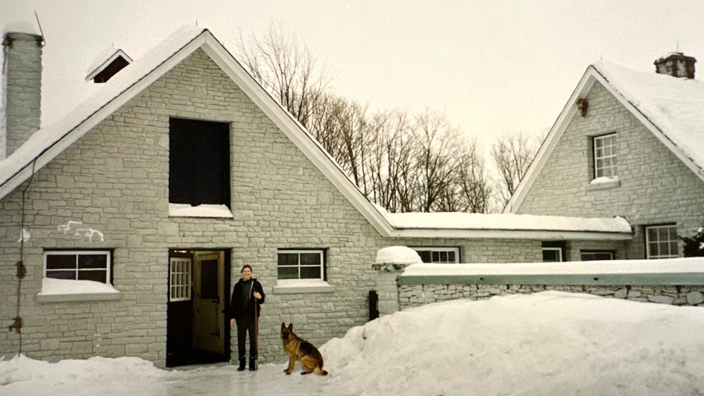A woman and dog standing outside a grey barn.