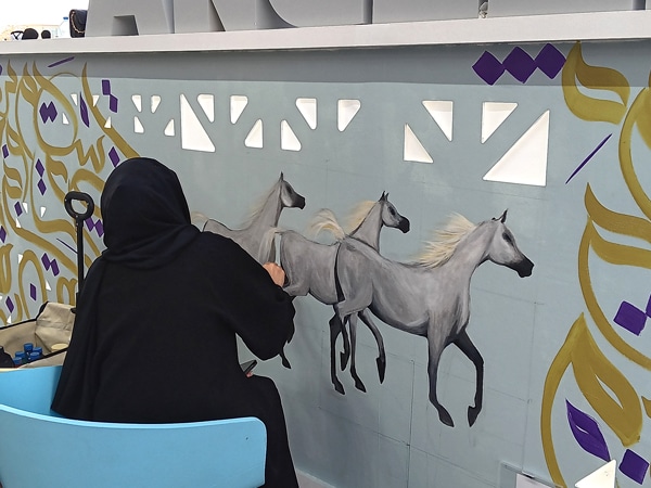 A woman painting horses on a wall.