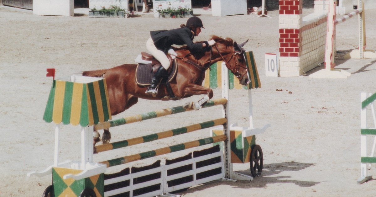 An old photo of a horse and rider jumping a fence in competition.