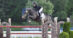 A woman on a dark grey horse jumping a fence in Kentucky.