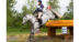 A rider and grey horse dropping into a water jump at Bromont.