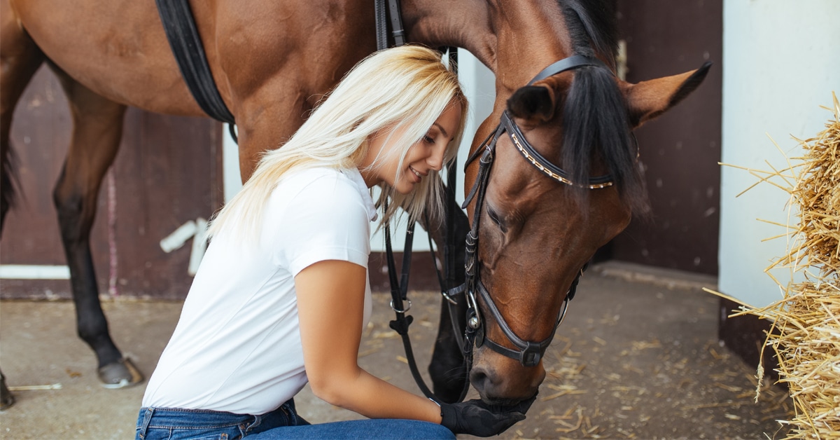 A woman kneeling with a horse sniffing her hand.