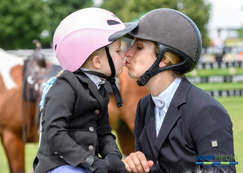 A woman kissing a baby wearing a pink riding helmet. 