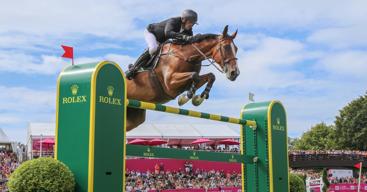 A man jumping a bay horse over a Rolex fence in France.