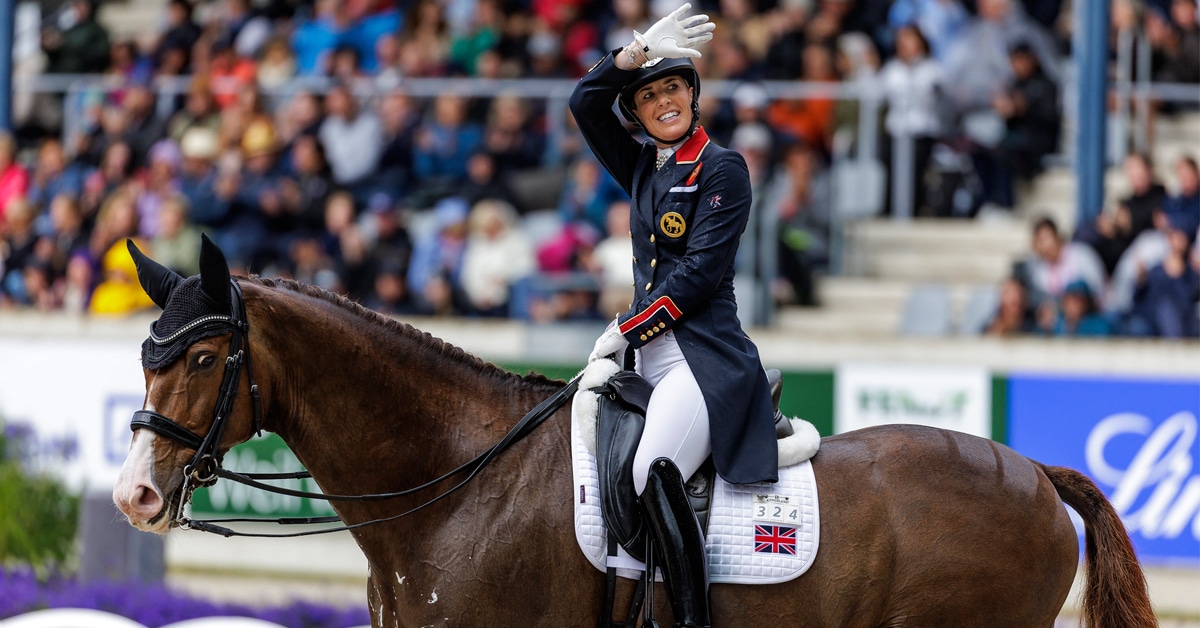 A woman waving from the back of a dressage horse.