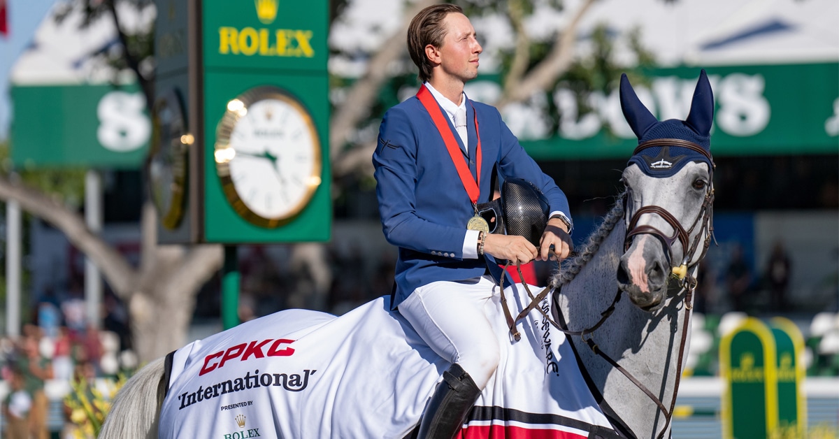 A man in a ble jacket sitting on a grey horse at Spruce Meadows.